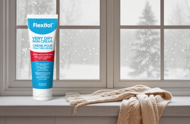 Tube of Flexitol Very Dry Skin Cream on a windowsill with a cozy scarf, snowy background outside.