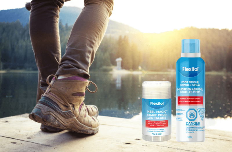 Flexitol Heel Magic jar and Flexitol Foot Odour Powder Spray bottle on a wooden dock near someone wearing hiking boots